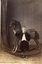 Dreng stående og holder tøjler af en gyngehest, 1860